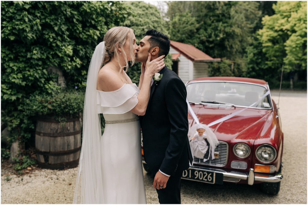 bride groom kissing white dress black suit vineyard trents christchurch wedding photographer classic car red cloudy day summer