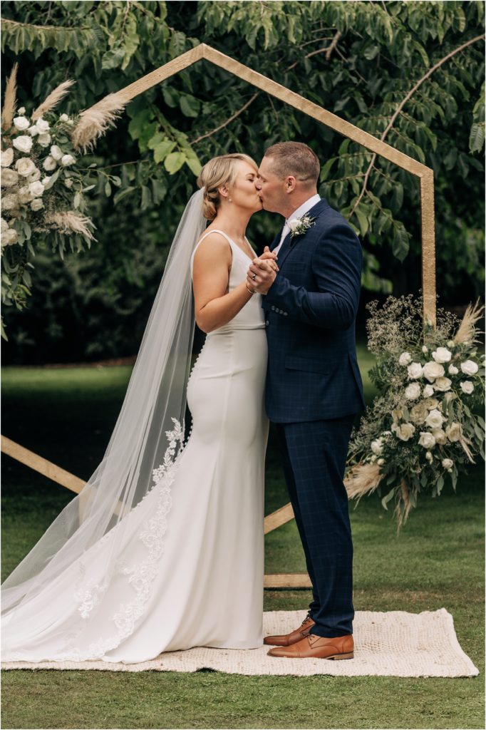 bride and groom first kiss in garden hexagonal archway with fresh flowers christchurch summer wedding nz
