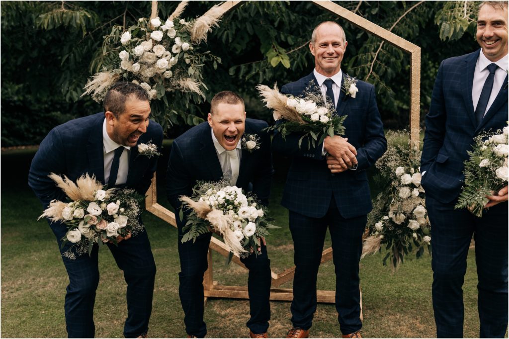 groomsmen in navy suits in front of hexagonal arch holding flowers bouquets christchurch wedding 