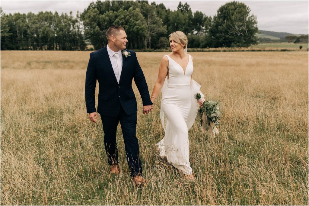 bride and groom white flowers navy suit in long dry grass summer wedding christchurch classic elegant holding hands