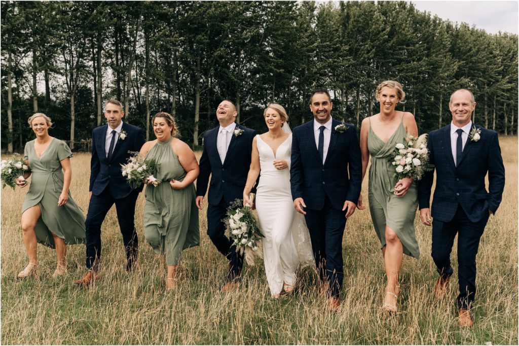 bridal party sage green bridesmaids with white flowers navy suits groomsmen walking through dry grass christchurch nz 