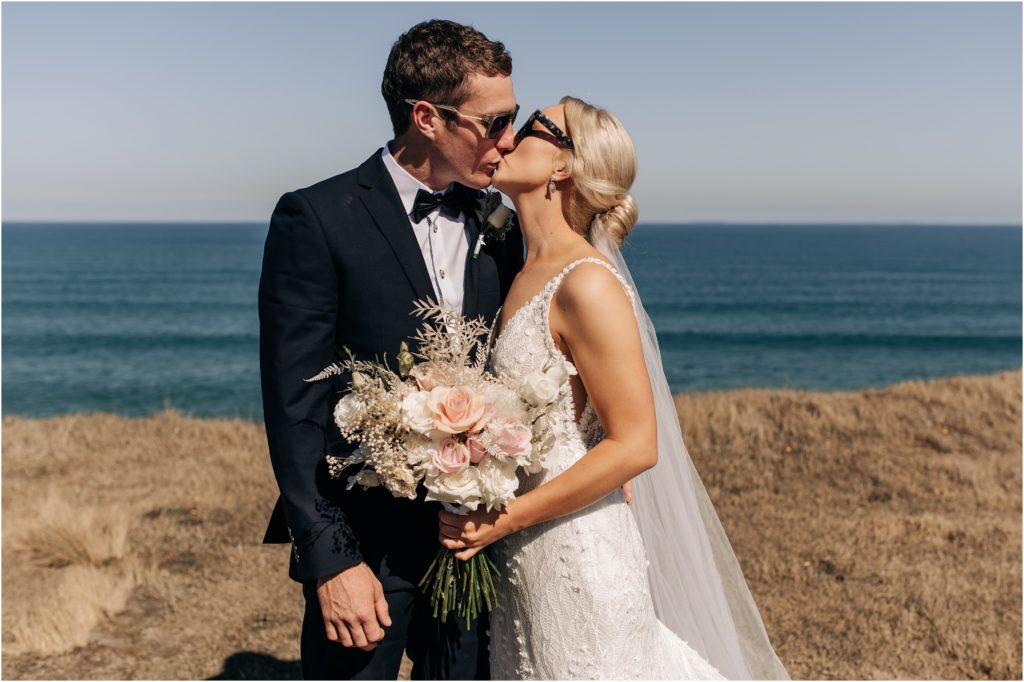 bride and groom on cliffs at fortrose kissing with sunglasses sunny day catlins new zealand wedding photographer christchurch 