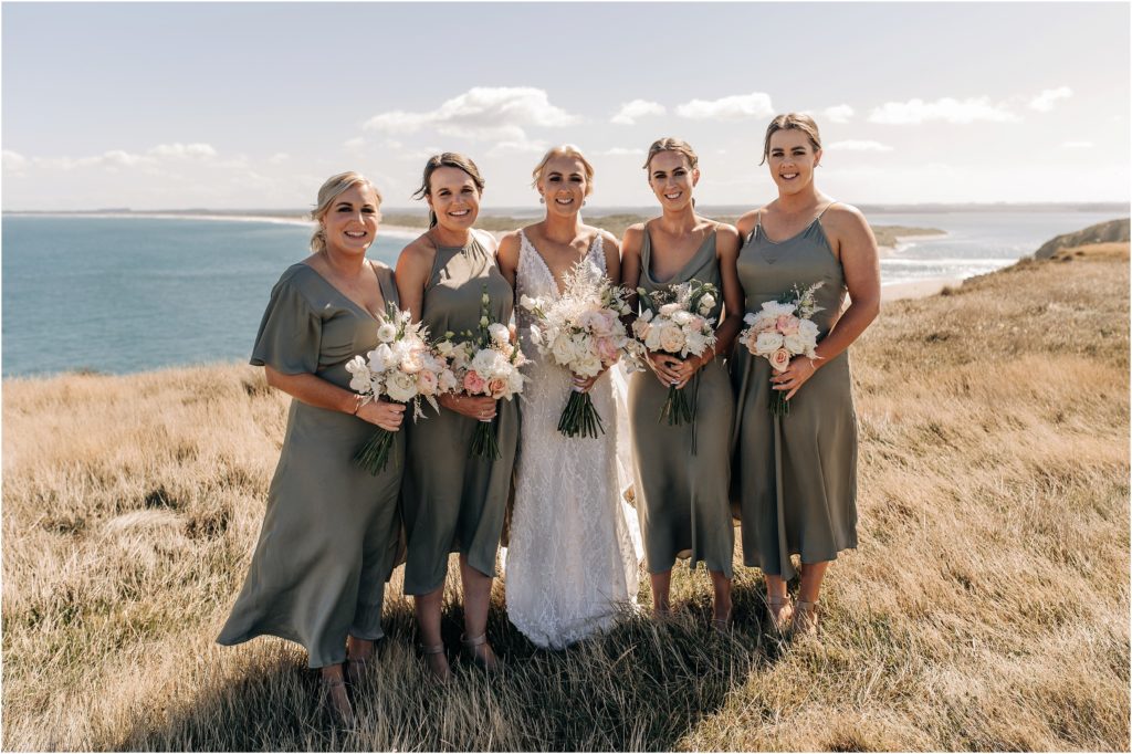 bride and bridesmaids in sage green catlins new zealand wedding photographer christchurch on cliffs sunny day ocean in background