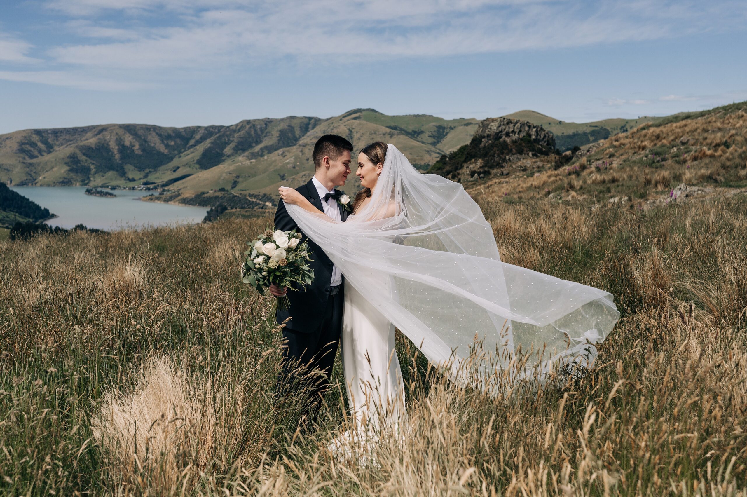 bride and groom on a mountaintop overlooking port levy in new zealand